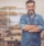 Carpenter in wood workshop. Mature man in casual clothing. Space is full of working tools and wooden planks.